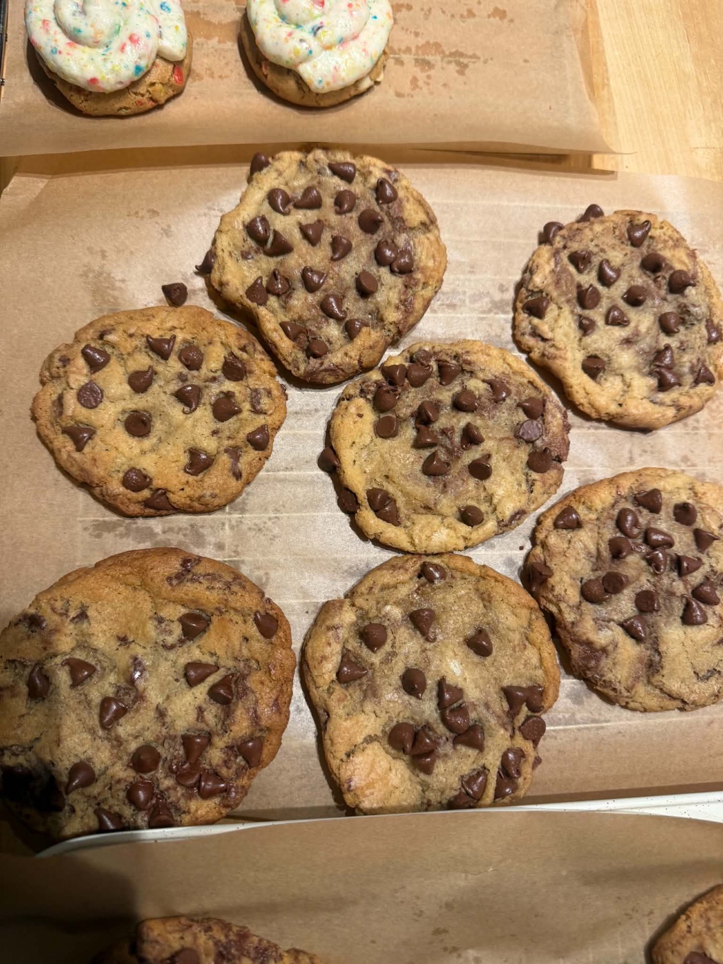 Chocolate chip cookies and colorful cookies arranged on parchment-lined trays