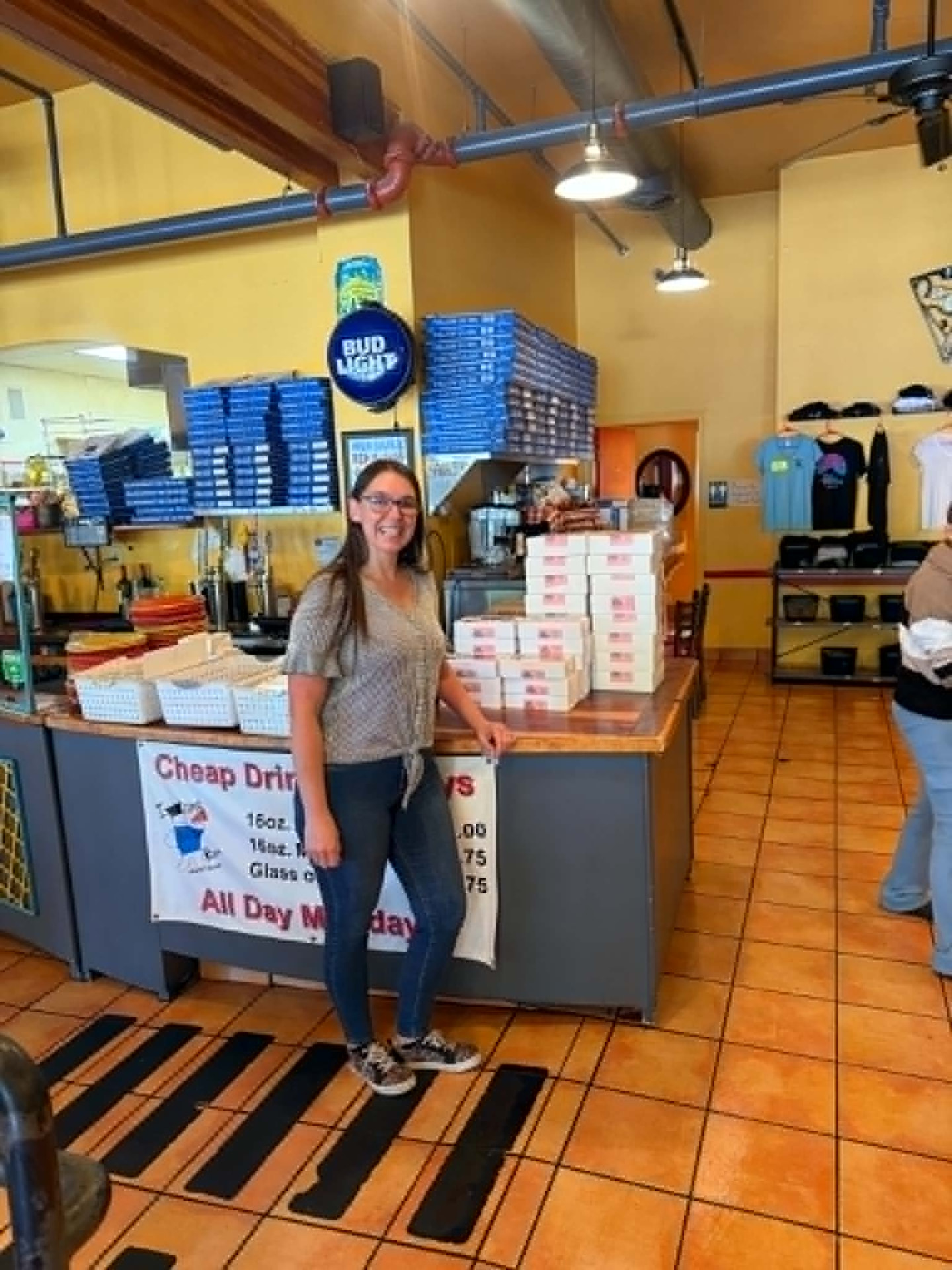 Tiffany Alford standing beside a display of Mommy & Me Goodies cookie boxes at Bill's Pizza