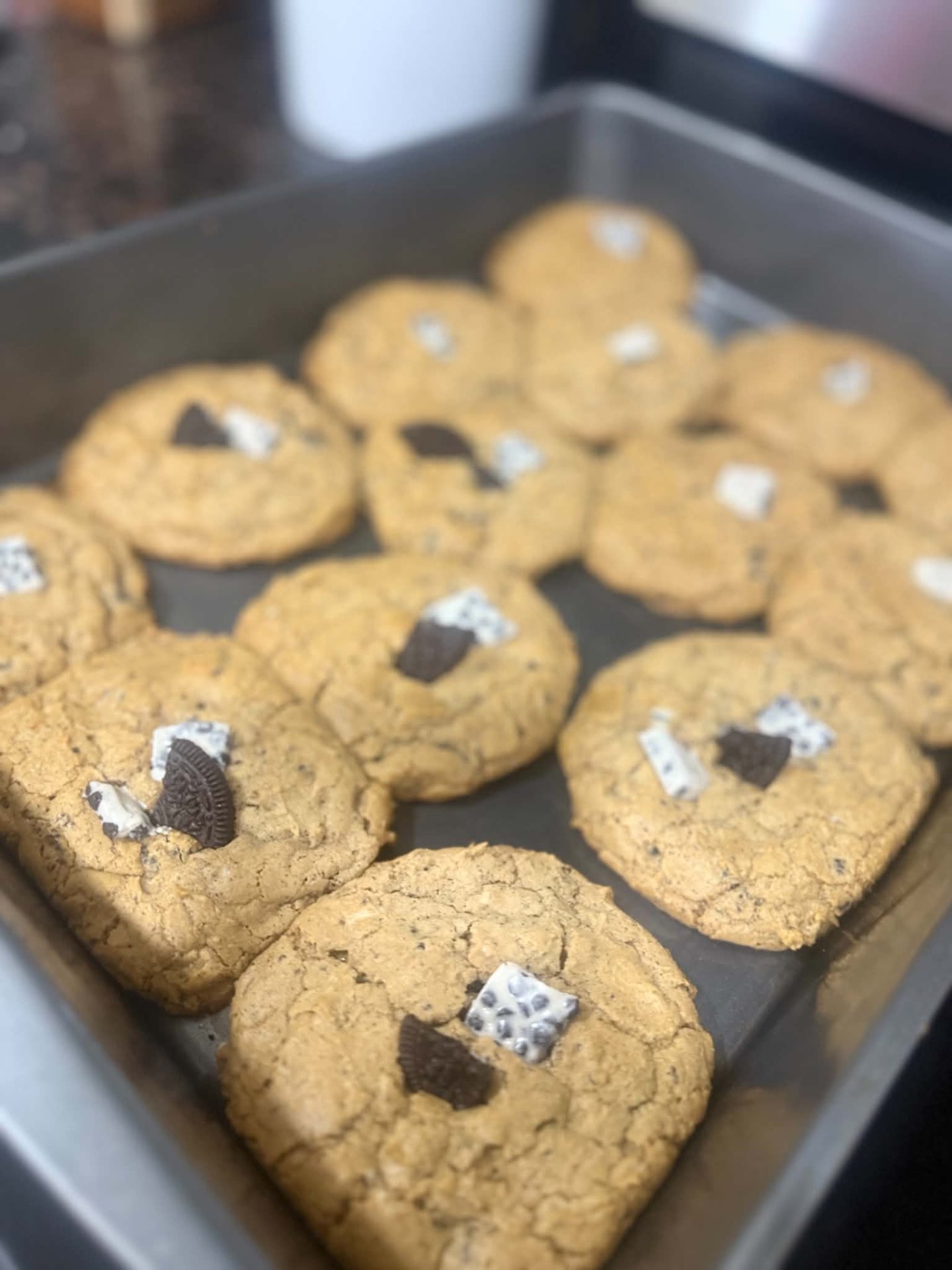 Fresh cookies topped with pieces of chocolate sandwich cookies on a baking tray