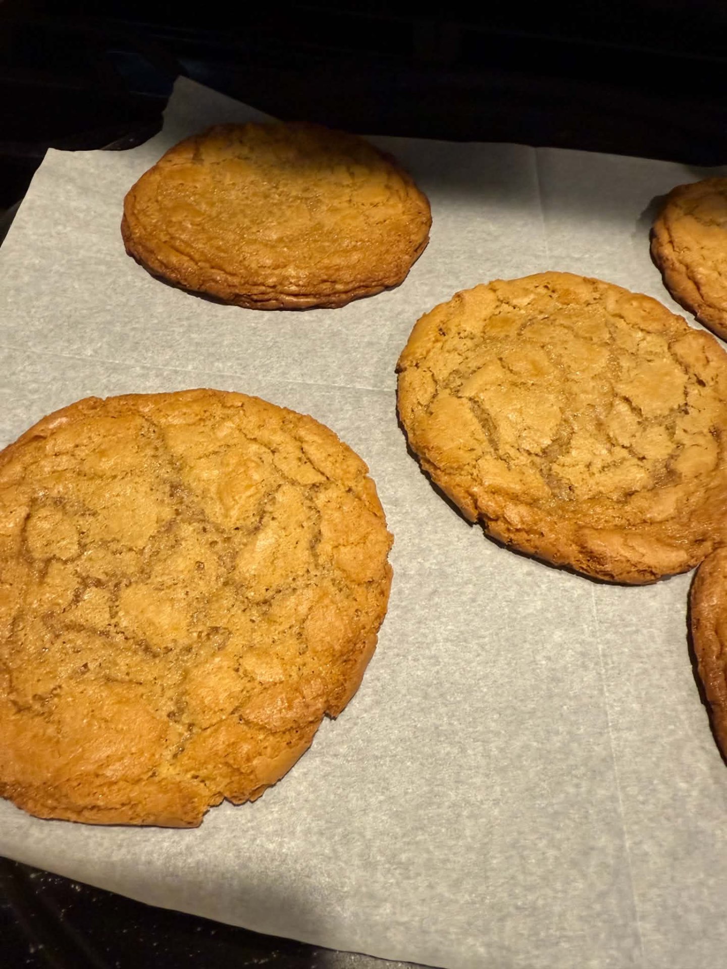 Large golden homemade cookies cooling on parchment paper