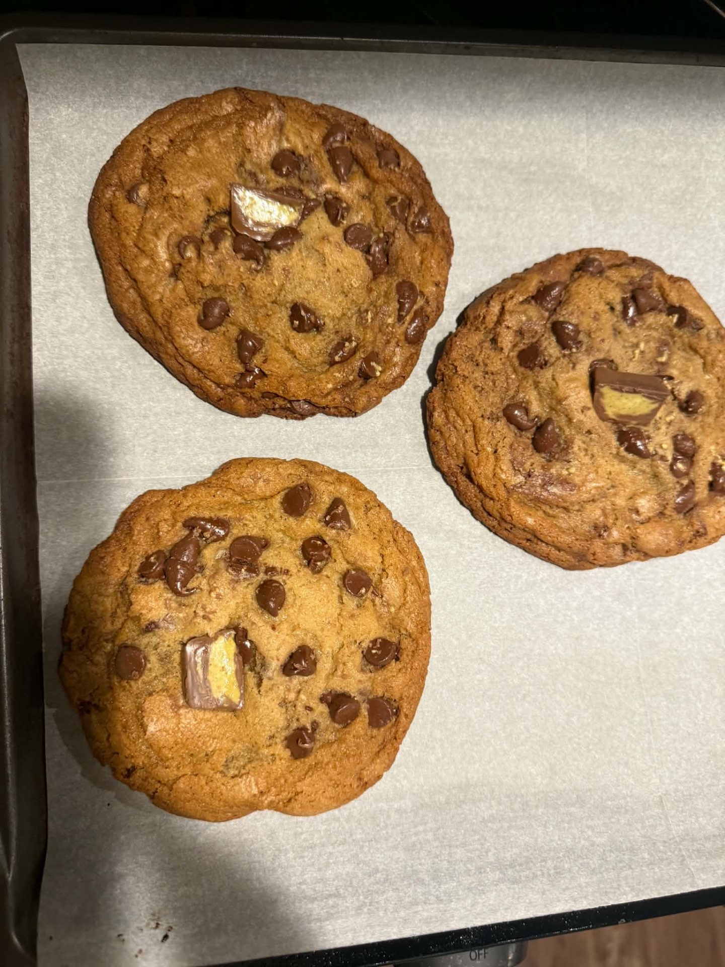 Three large homemade cookies topped with chocolate chips and chocolate candy pieces